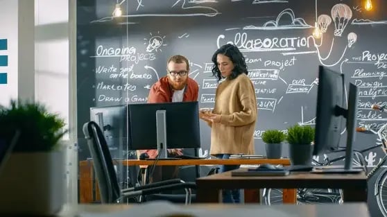 Diseñadora habla con desarrollador mientras miran la pantalla de un ordenador personal.